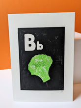 Load image into Gallery viewer, A black and white print with a green broccoli printed on, with an orange background
