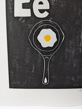 Load image into Gallery viewer, A close up of a black print of a fried egg in a black frying pan
