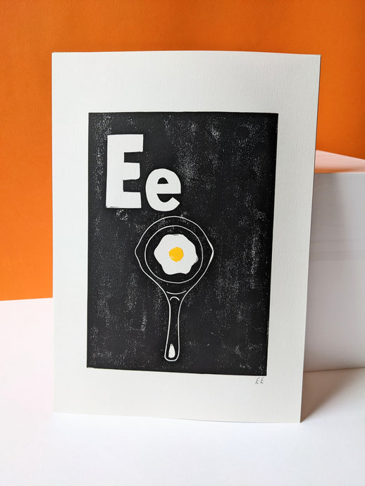 A black print with a fried egg in a pan against on orange background