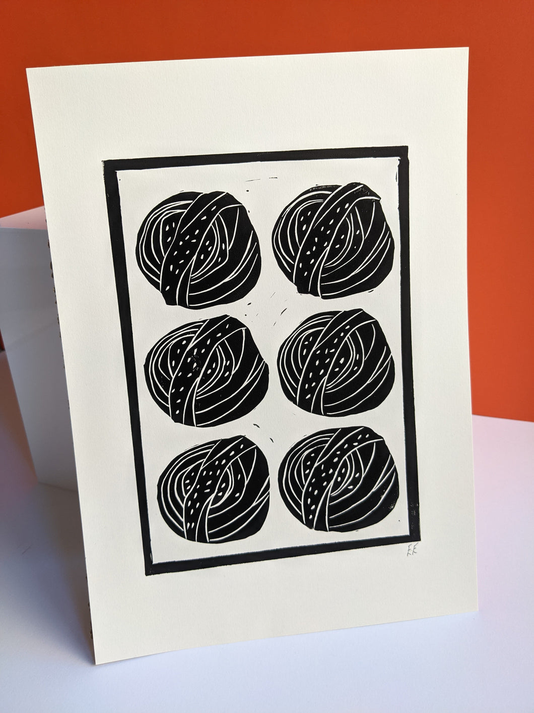 A black and white print of six cinnamon buns against an orange background