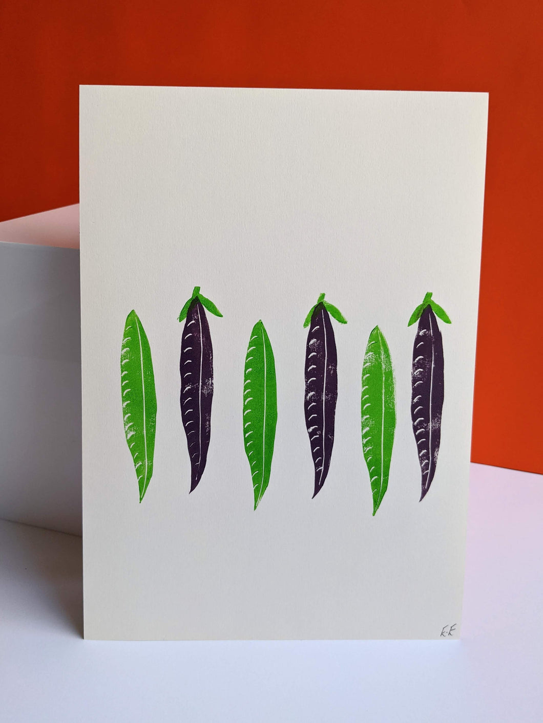 A print of three green pea pods and three purple pea pods against an orange background