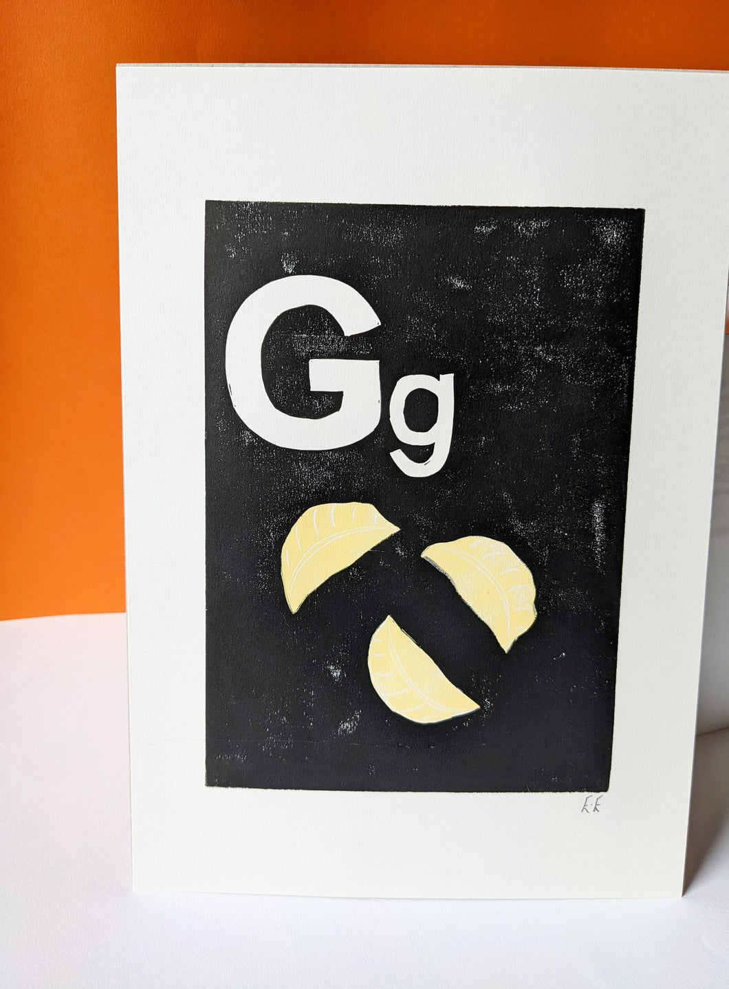 A black and cream print of three gyoza dumpling against an orange background