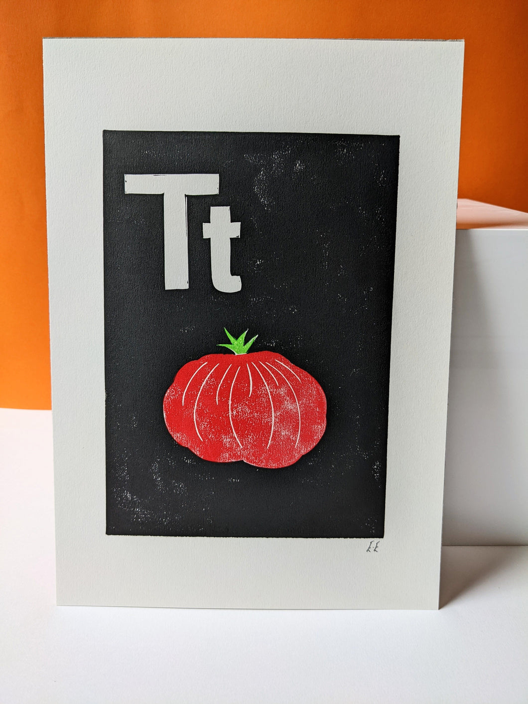 A black print with a red tomato and the letter T carved out of it in white
