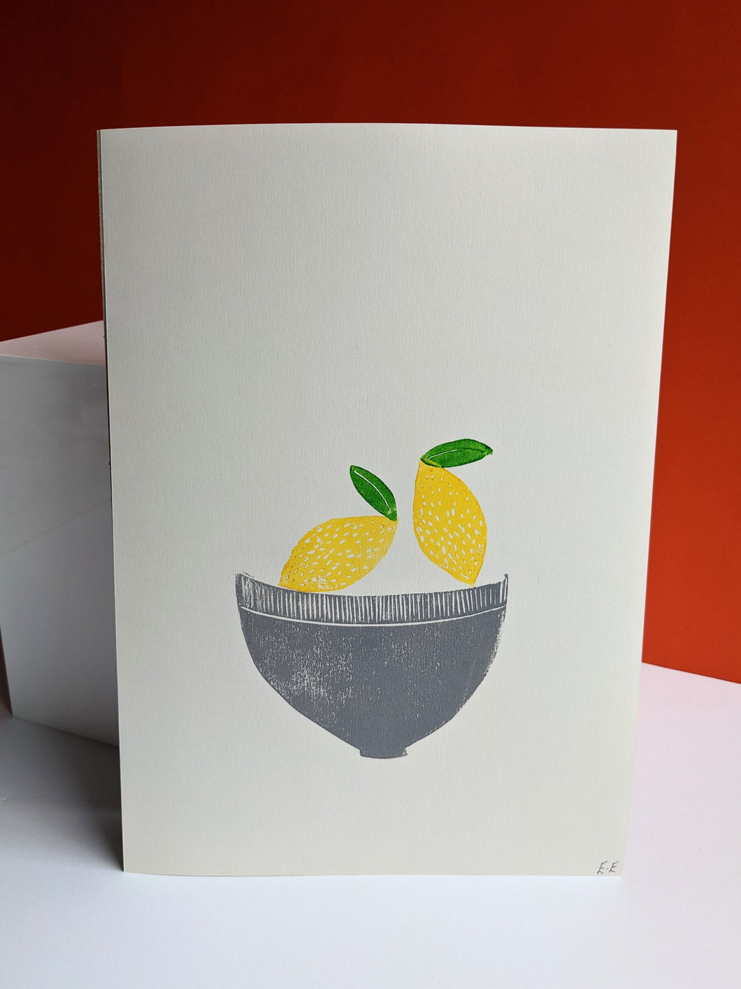 A print of a grey bowl with two yellow lemons each with a green leaf